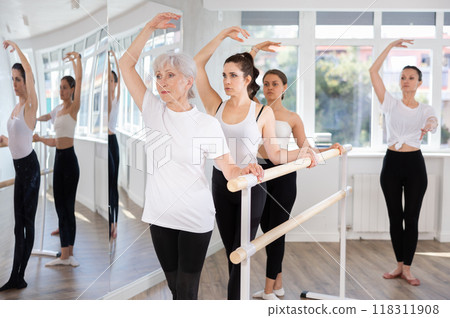 Women exercise near the ballet barre at group training session in fourth position in dance studio Women exercise near the ballet barre at group training session in fourth position in dance studio 118311908