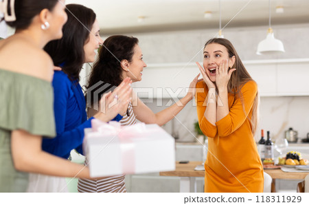 Joyful young woman greeting friends bearing present at home celebration 118311929