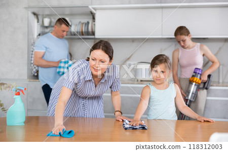 Cheerful woman wiping table in kitchen with preteen daughter Cheerful woman wiping table in kitchen with preteen daughter 118312003