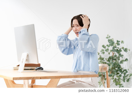 A woman holding her head looking at a computer A woman holding her head looking at a computer 118312060