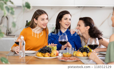 Four women are sitting at table, enjoying food and wine, chatting, talking, laughing. 118312129