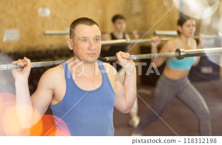 Motivated CrossFit middle-aged male athlete lifting heavy body bar or barbell during group training in gym. Functional training concept 118312198