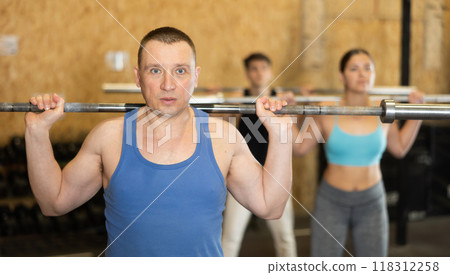 Energetic male athlete practicing sit-ups with rod near other people gym Energetic male athlete practicing sit-ups with rod near other people gym 118312258
