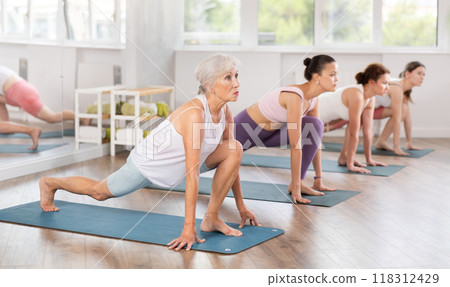 Elderly woman performing Lunge Equestrian Pose in yoga studio 118312429