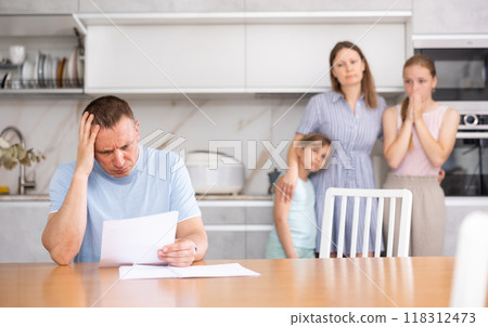 Upset worried man sitting with papers at kitchen table 118312473
