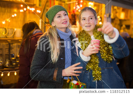 Daughter points her hand to mom as they walk through street Christmas market Daughter points her hand to mom as they walk through street Christmas market 118312515