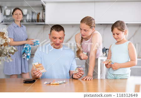 Teenage sisters asking for pocket money from smiling father at home Teenage sisters asking for pocket money from smiling father at home 118312649