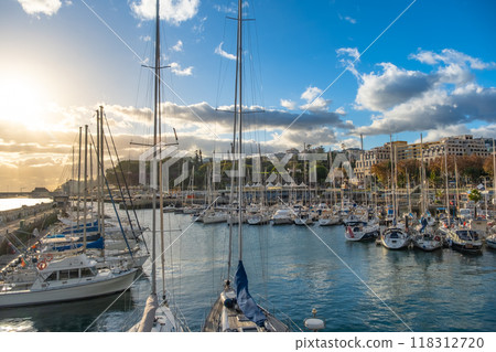 A stunning view of a Funchal marina on Madeira island filled with boats, yachts and sailboats under a beautiful sunset in a lively coastal city 118312720