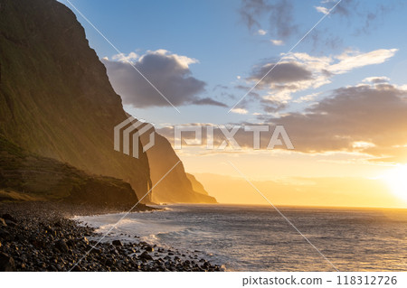 Volcanic rock cliffs Achadas da Cruz in backlit sunlight. Waves of the Atlantic Ocean. Beautiful sunset seascape of the resort island of Madeira, Portugal Volcanic rock cliffs Achadas da Cruz in backlit sunlight. Waves of the Atlantic Ocean. Beautiful sunset seascape of the resort island of Madeira, Portugal 118312726