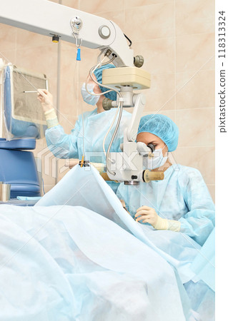 Surgeons performing precision ophthalmic surgery with advanced medical equipment Surgeons performing precision ophthalmic surgery with advanced medical equipment 118313324
