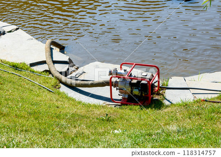 Water pump with a hose on the bank of a pond. 118314757