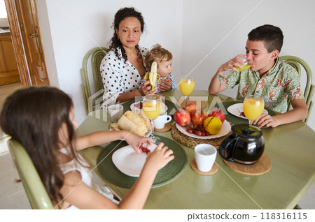 A family shares a nutritious breakfast featuring fresh fruits, juice, and bread, capturing a moment of togetherness and warmth in their home. 118316115