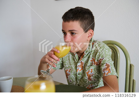 A boy in a stylish tiger-print shirt sipping orange juice from a wine glass while seated at a table. The casual setting suggests a relaxed atmosphere. A boy in a stylish tiger-print shirt sipping orange juice from a wine glass while seated at a table. The casual setting suggests a relaxed atmosphere. 118316129