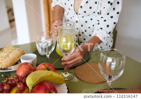 A woman sets a breakfast table with fresh fruits, bread, and juice. The scene captures a cozy home atmosphere and promotes healthy living and mindful morning routines. A woman sets a breakfast table with fresh fruits, bread, and juice. The scene captures a cozy home atmosphere and promotes healthy living and mindful morning routines. 118316147