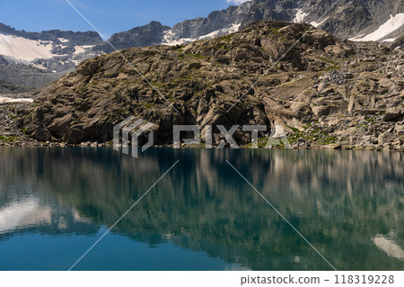 Clear mountain lake reflecting rocky cliffs and snow capped peaks 118319228