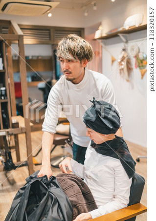 The hairdresser removes the blanket, turns the chair and guides the customer to the shampoo station. 118320157