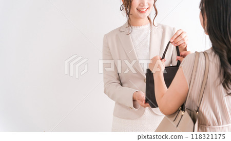 一名店員/銷售人員和一名女性購物者在奢侈品店（百貨公司、百貨公司、品牌商品）遞紙袋和產品 118321175