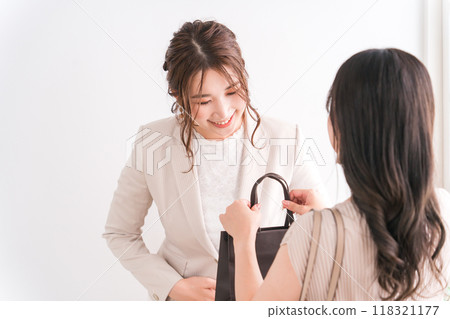 A shop clerk/salesperson and a female shopper handing over paper bags and products at a luxury store (department store, department store, branded goods) 118321177