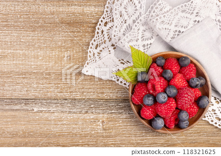 Plate with raspberries and blueberries on the wooden table with laced cloth. 118321625
