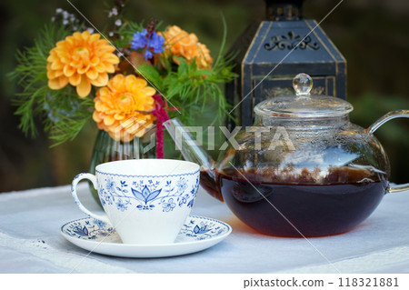 Patio table with cup of tea, pot, flowers and lantern. 118321881