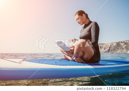 Woman sea laptop. Digital nomad, freelancer with laptop working on sup board at calm sea beach. Happy smiling girl relieves stress from work. Freelance, digital nomad, travel and holidays concept 118322794