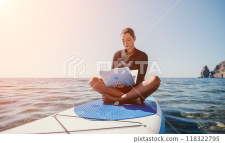Digital nomad, freelancer, laptop. Happy smiling woman working on sup board at calm sea beach, relieves stress from work. Freelance, remote work on vacation, travel and holidays concept. Digital nomad, freelancer, laptop. Happy smiling woman working on sup board at calm sea beach, relieves stress from work. Freelance, remote work on vacation, travel and holidays concept. 118322795