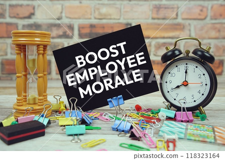 Boost Employee Morale text on paper card with alarm clock and stationary on wooden background Boost Employee Morale text on paper card with alarm clock and stationary on wooden background 118323164