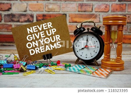 Never Give Up On Your Dreams text on paper card with alarm clock and stationary on wooden background 118323395