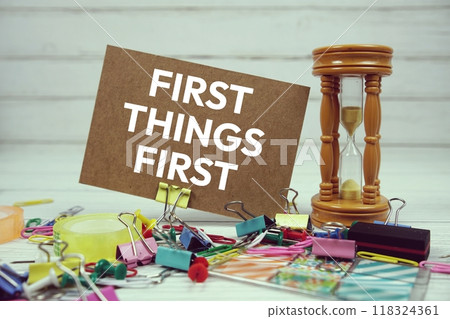First Things First text on paper card with hourglass and stationary on wooden background First Things First text on paper card with hourglass and stationary on wooden background 118324361