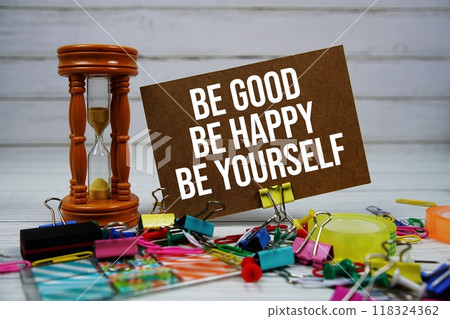 Be Good Be Happy Be Yourself text on paper card with hourglass and stationary on wooden background Be Good Be Happy Be Yourself text on paper card with hourglass and stationary on wooden background 118324362