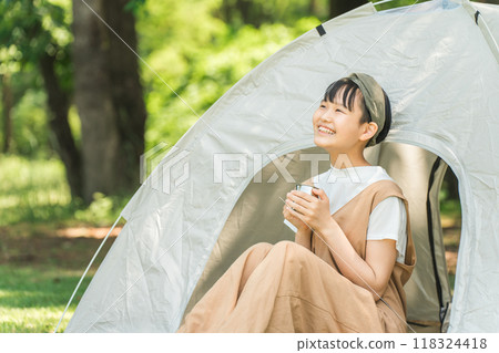 A girl drinking a drink in front of a tent at a campsite or leisure facility A girl drinking a drink in front of a tent at a campsite or leisure facility 118324418