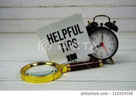 Helpful Tips text on paper card with alarm clock and magnifying glass on wooden background 118324598