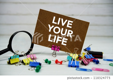 Live Your Life text on paper card with magnifying glass and stationary on wooden background 118324773