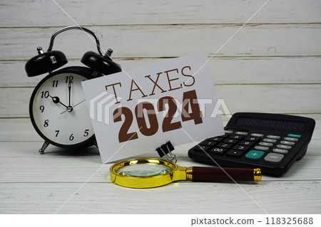 Taxes 2024 text on paper card with alarm clock, calculator and magnifying glass on wooden background Taxes 2024 text on paper card with alarm clock, calculator and magnifying glass on wooden background 118325688