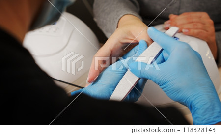 Nail care at home. Process of nail treatment in a nail salon. A view from behind the nail master shoulder of the nail care process. 118328143