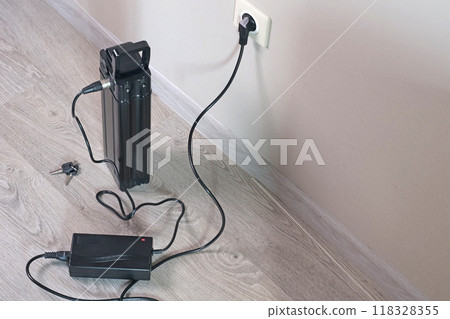 Charging bicycle battery from mains electricity in house. Socket in room with plug switched on. Environmentally friendly transport.  118328355