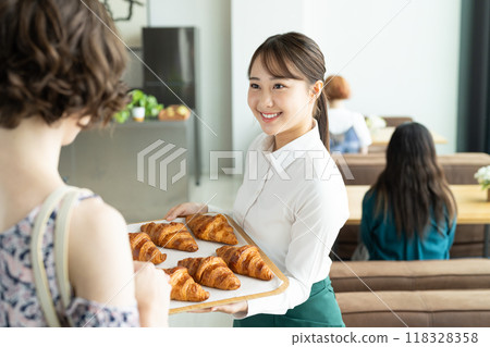 A young female sales clerk recommending a croissant 118328358