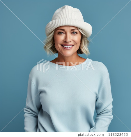 Happy middle aged woman in a beige winter hat and a blue sweater. Portrait of beautiful mature woman in a winter cap smiling on a blue background looking at camera. Cheerful caucasian woman in a hat. 118328453