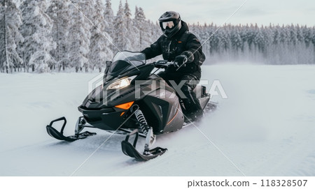 A man riding on a snowmobile through a snowy forest on a sunny winter day. Guy riding outside on a cold winter day. A man is riding on a snow mobile in a snowy forest. 118328507