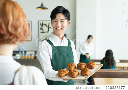 A young male store clerk recommending freshly baked bread to a customer 118328677