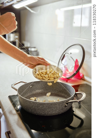 Cooking with care as cashews are added to a hot pan in a modern kitchen setup Cooking with care as cashews are added to a hot pan in a modern kitchen setup 118330270