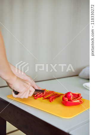 Slicing vibrant red bell peppers on a yellow cutting board in a cozy kitchen setting Slicing vibrant red bell peppers on a yellow cutting board in a cozy kitchen setting 118330272