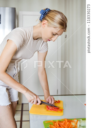 Woman skillfully chopping vegetables in a bright kitchen during midday preparations Woman skillfully chopping vegetables in a bright kitchen during midday preparations 118330273