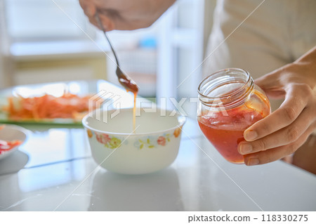 Unrecognizable woman carefully pours sweet chilli sauce from a small jar into a bowl while preparing for a meal 118330275