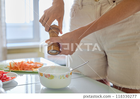 Person preparing a meal by grinding pepper over a bowl in a bright kitchen during the day Person preparing a meal by grinding pepper over a bowl in a bright kitchen during the day 118330277