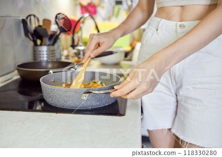 A person cooking vegetables in a frying pan in a bright kitchen setting during the day 118330280