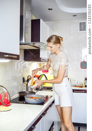 Young woman cooking in a modern kitchen while preparing a meal on a sunny afternoon 118330285
