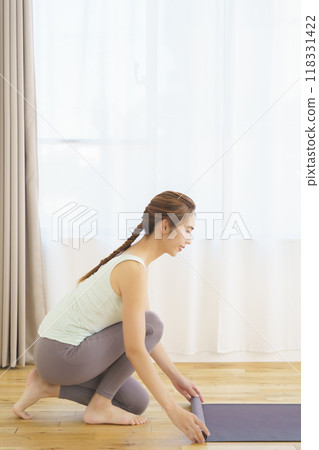 A young woman laying a mat in preparation for an online yoga salon A young woman laying a mat in preparation for an online yoga salon 118331422