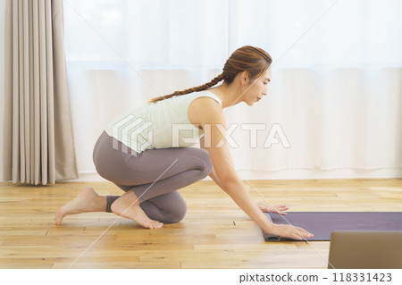 A young woman laying a mat in preparation for an online yoga salon 118331423
