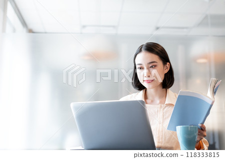 一位女士手裡拿著一本書操作電腦 一位女士手裡拿著一本書操作電腦 118333815